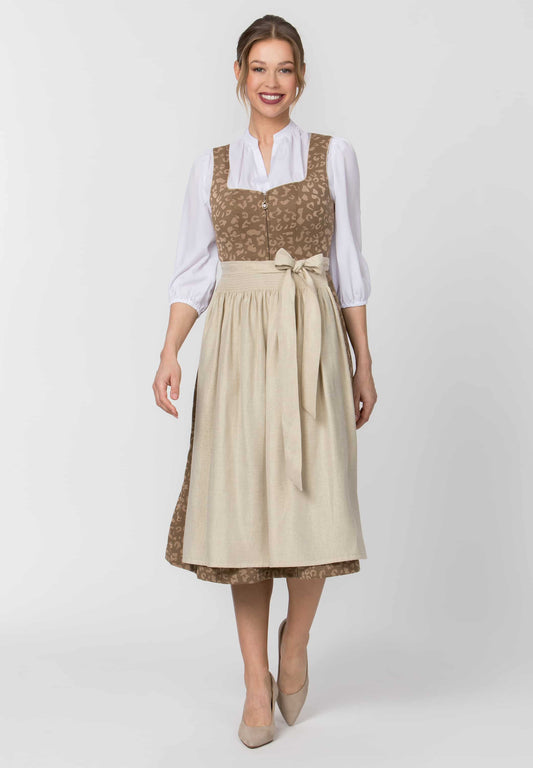 A woman modeling a traditional German dirndl dress with a beige skirt, brown patterned bodice, and a white blouse underneath, set against a plain light gray studio background.