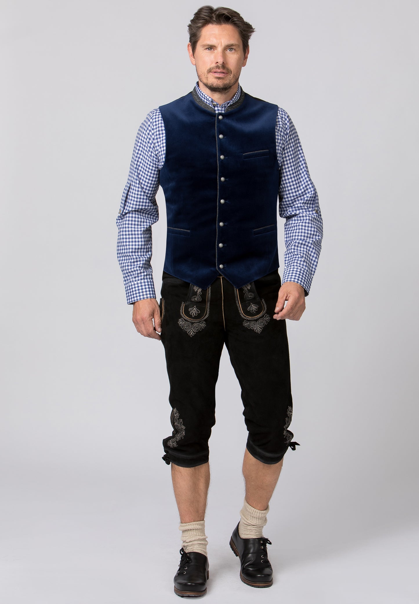 A full length view of a man wearing a traditional indigo blue men's vest with a stand-up collar, three pockets, and silver round knob buttons.