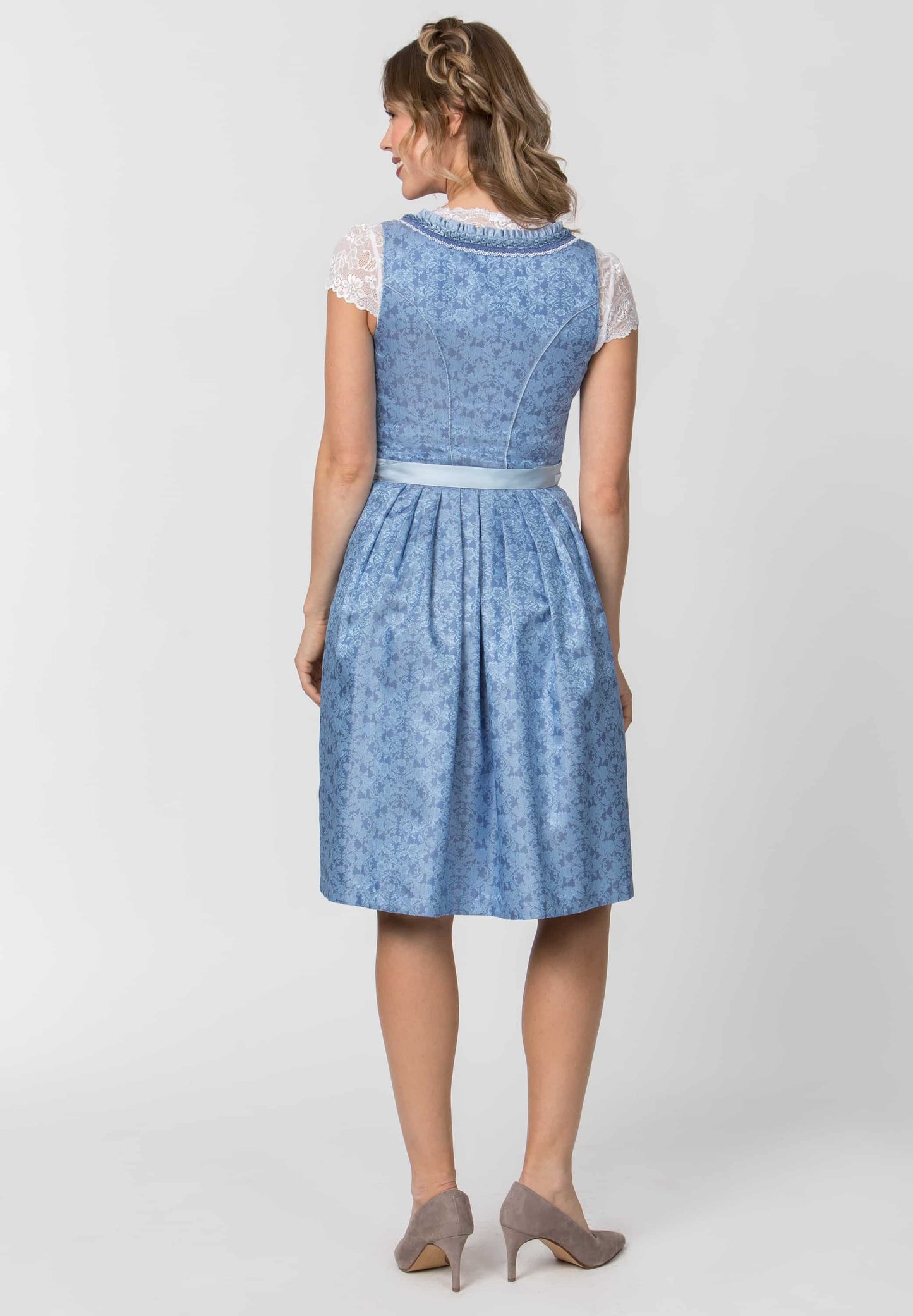 A woman modeling a light blue patterned dress with white lace sleeves and a matching waistband, shown from the back against a light gray studio background.