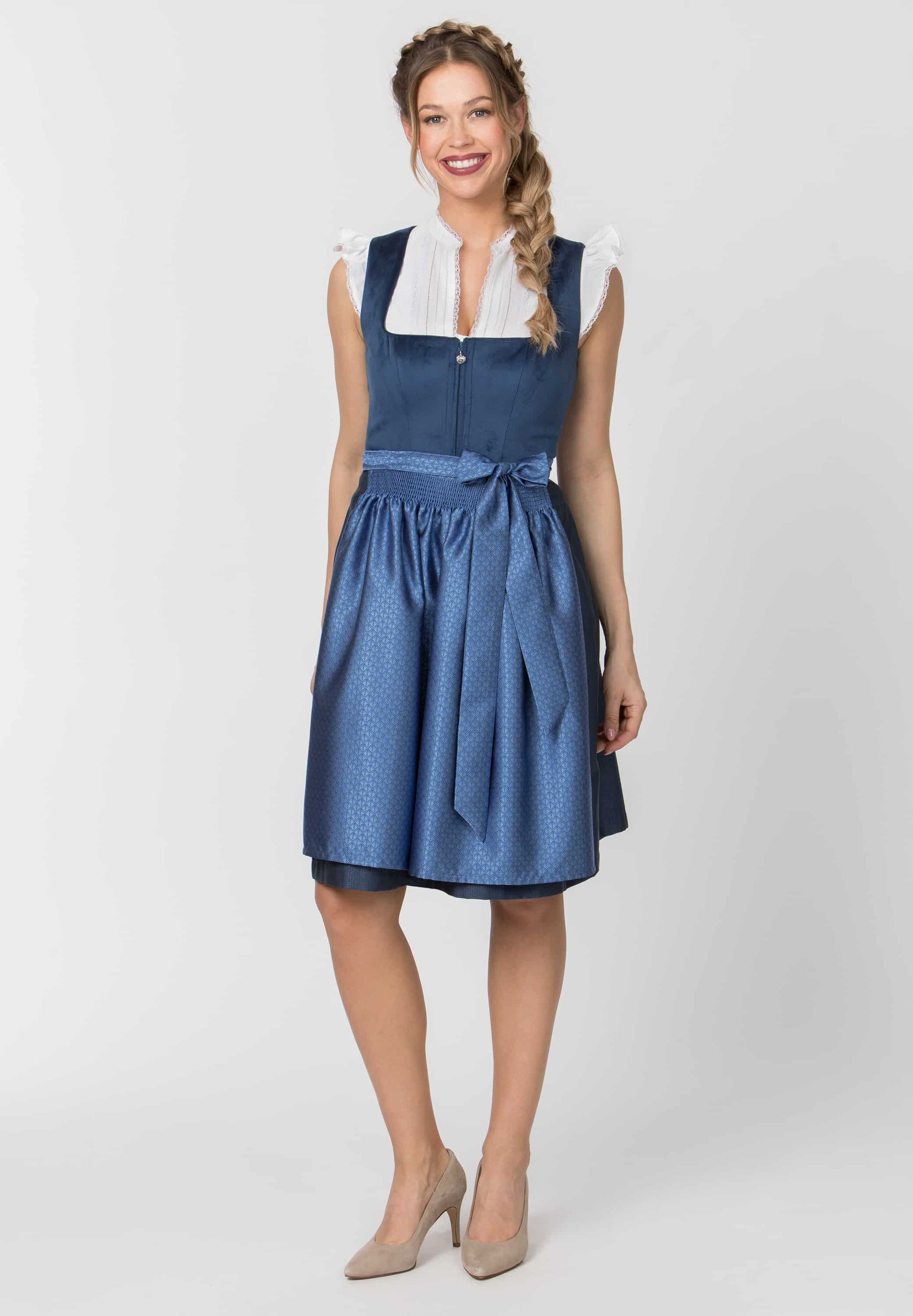 A woman modeling a sleeveless blue dress with a white collar and a matching blue waist tie, photographed against a light gray studio background.