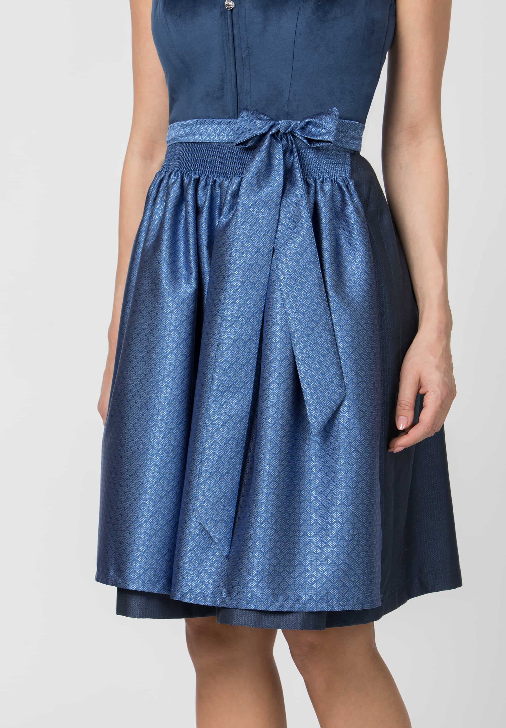 A woman wearing a blue sleeveless dress with a patterned skirt and matching waist tie, shown from the chest down against a light gray studio background.