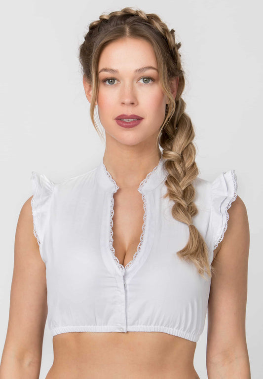 A woman with blonde braided hair wearing a white sleeveless crop top with ruffled shoulders and a lace-trimmed V-neck, photographed against a light gray studio background.