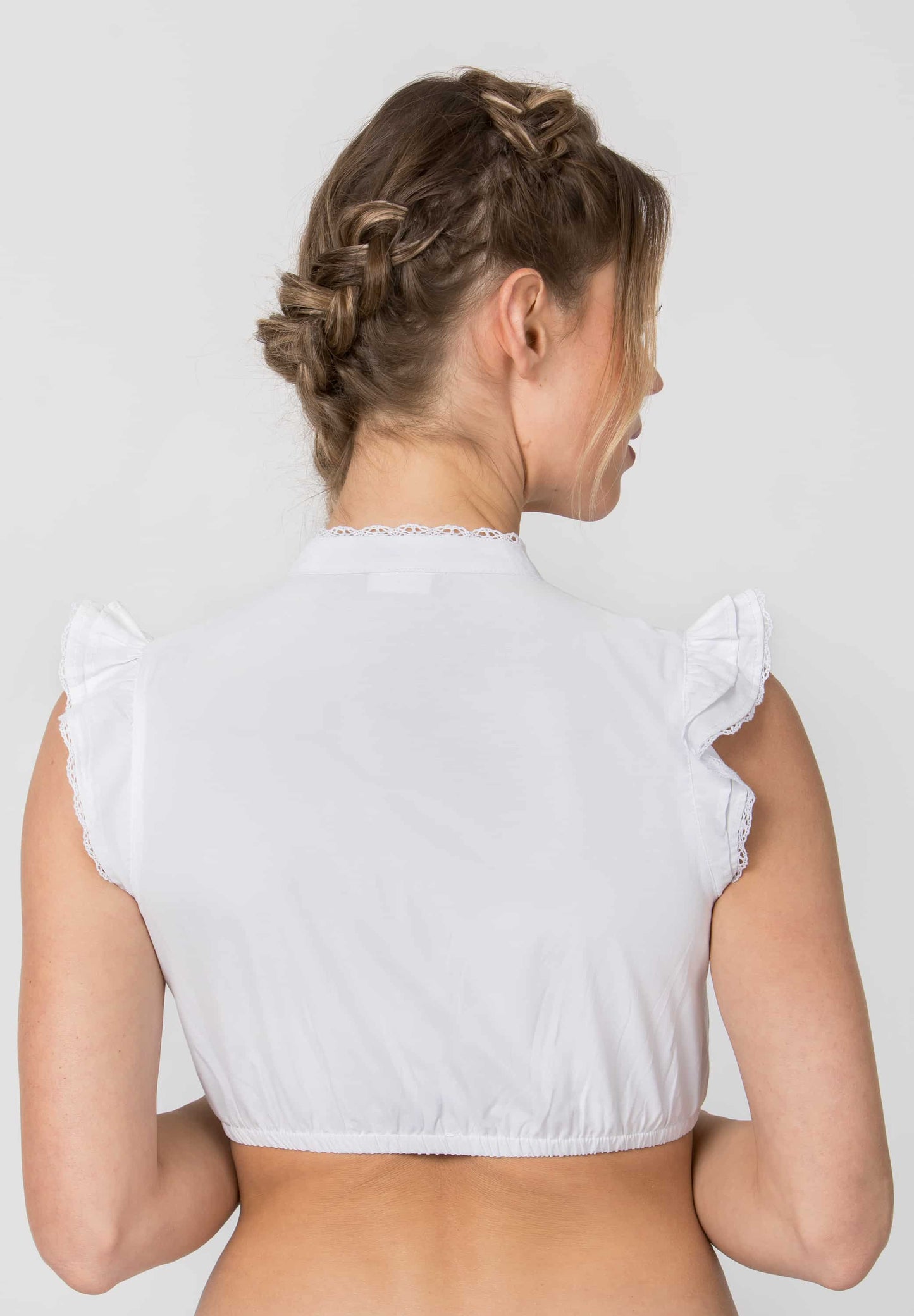Back view of a woman wearing a white sleeveless crop top with ruffled shoulders, shown against a light gray studio background.