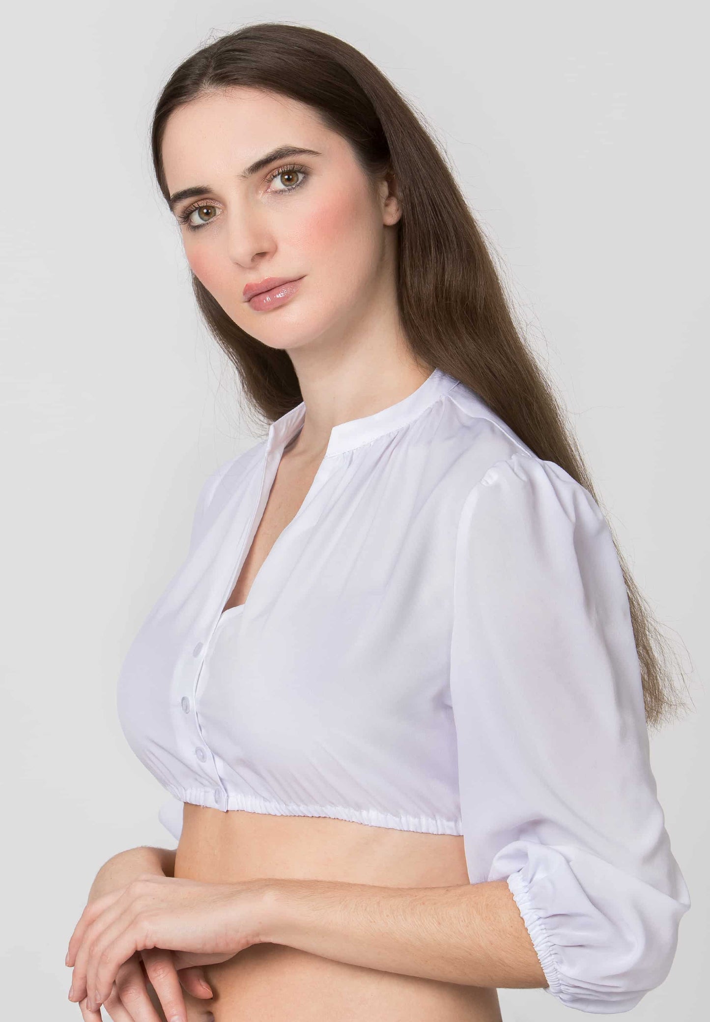 A woman modeling a white long-sleeve cropped blouse with a split neckline and gathered sleeves, photographed against a light gray studio background.