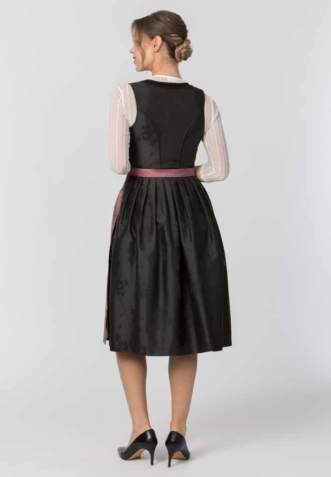 Woman wearing a black dress with the berry colored apron string showing at the waist with sheer sleeves on a white background