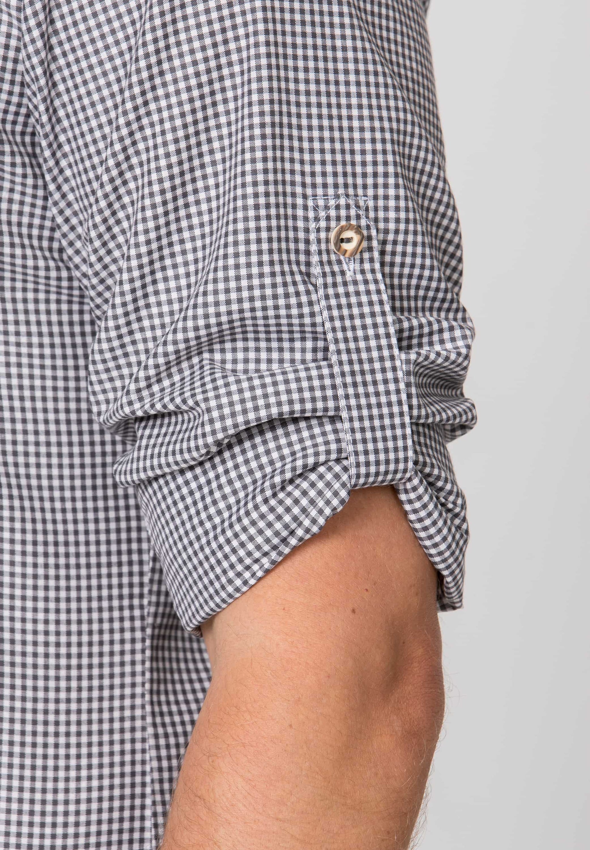 Close-up of a person wearing a black and white checkered shirt with rolled-up sleeves on a plain background