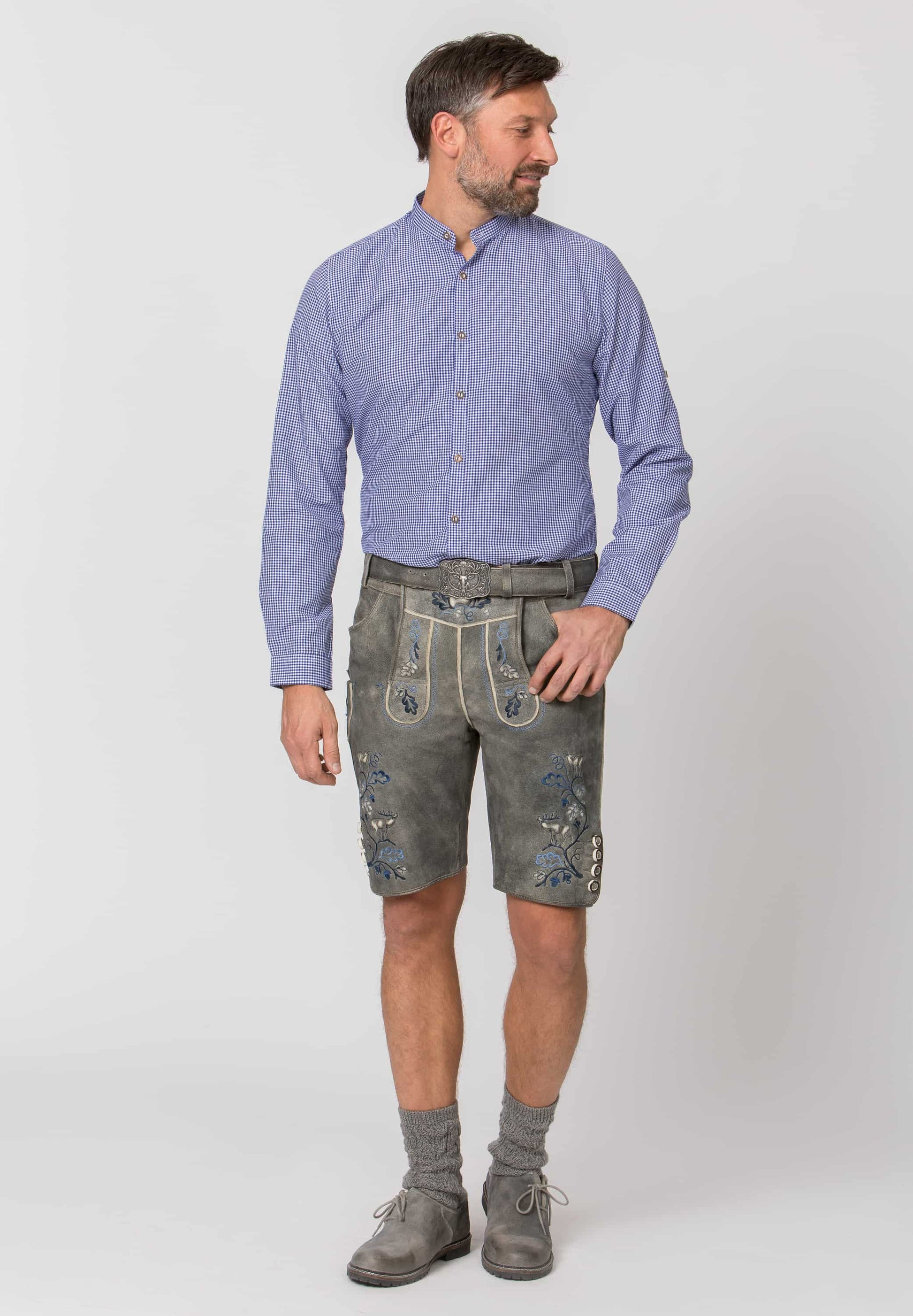Man wearing a blue shirt and gray traditional Bavarian shorts on a white background