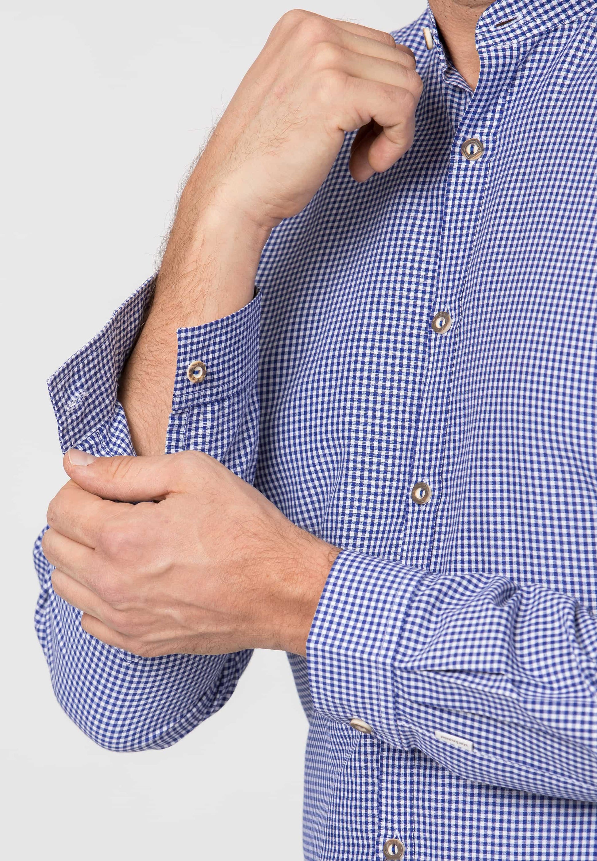 Person wearing a blue checkered shirt with rolled-up sleeves against a light gray background