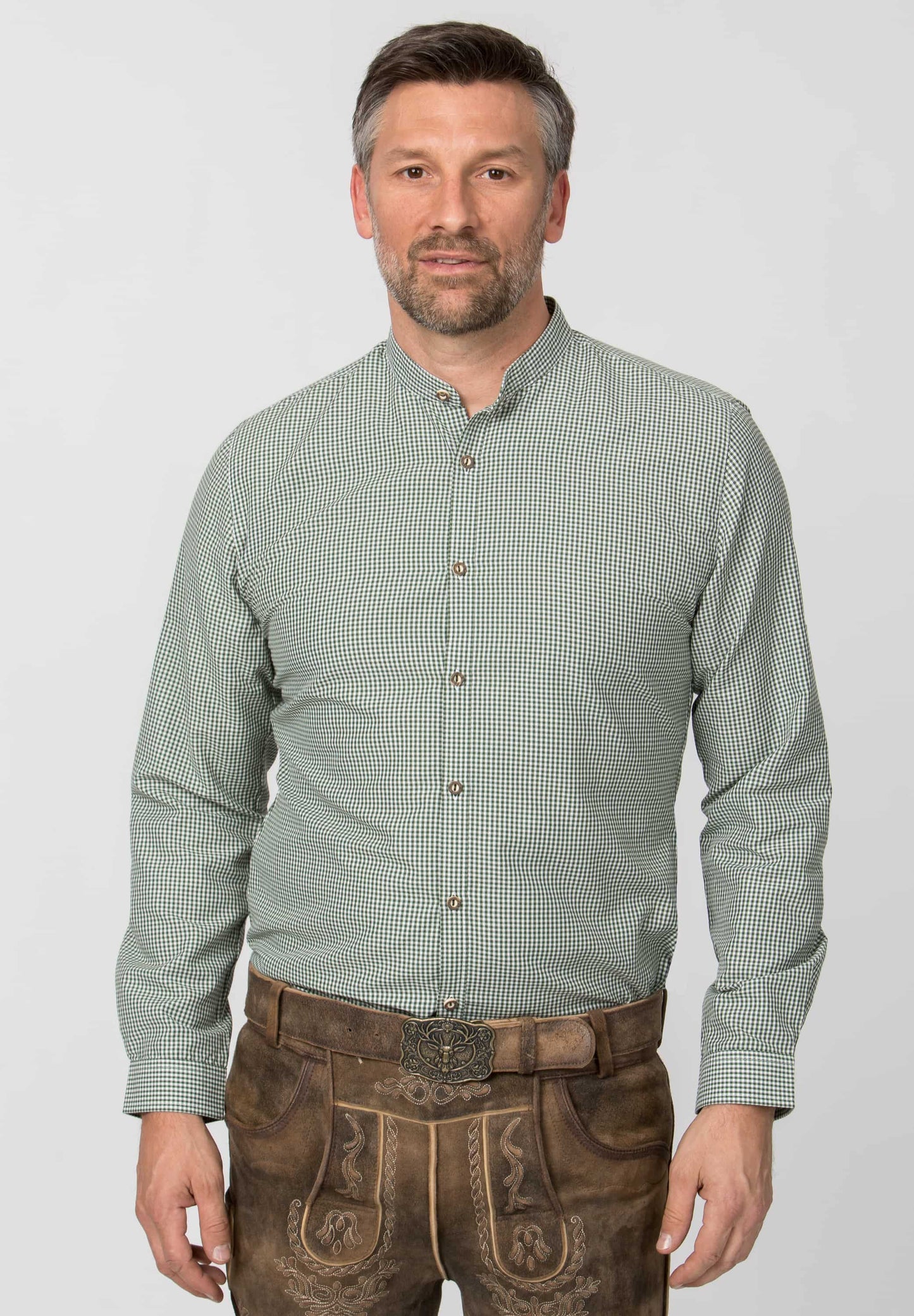 Man wearing a green checkered shirt and brown traditional pants on a white background