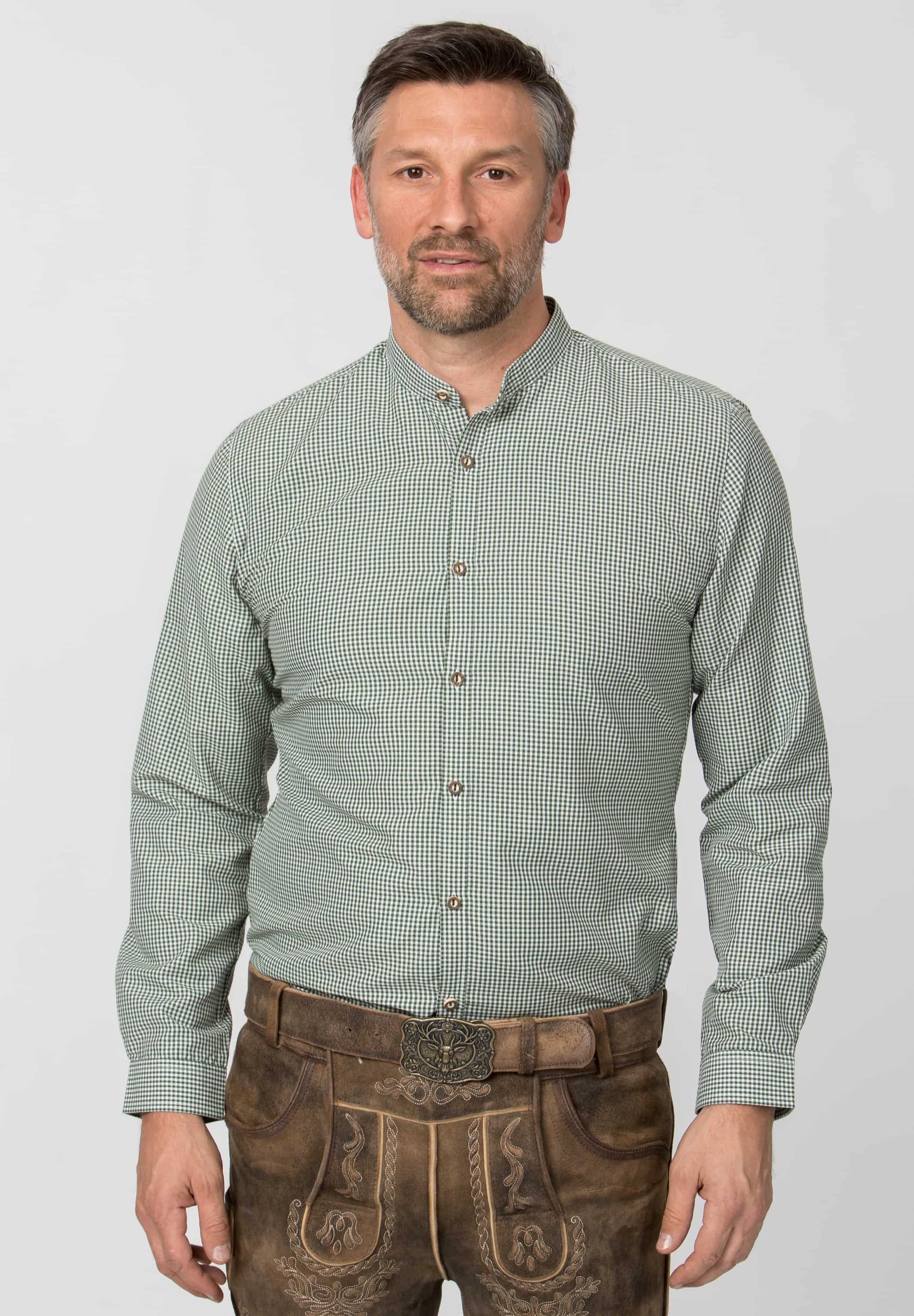 Man wearing a green checkered shirt and brown traditional pants on a white background