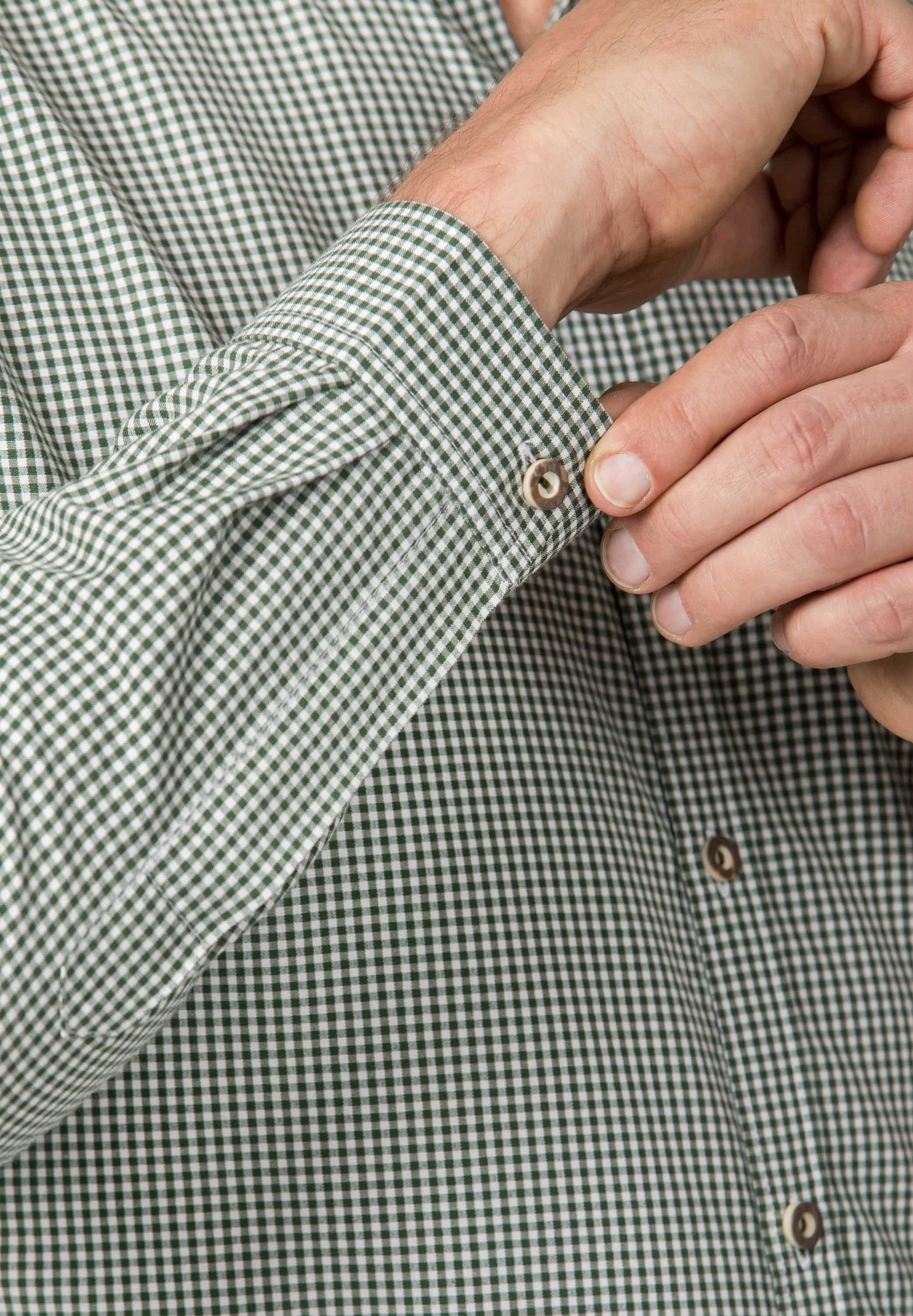 Close-up of a person adjusting the sleeve of a green and white checkered shirt.