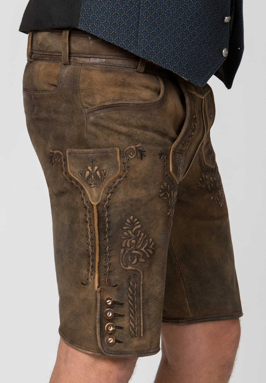 Close-up of a person wearing brown leather traditional shorts with embossed floral details and decorative stitching, paired with a dark patterned waistcoat.