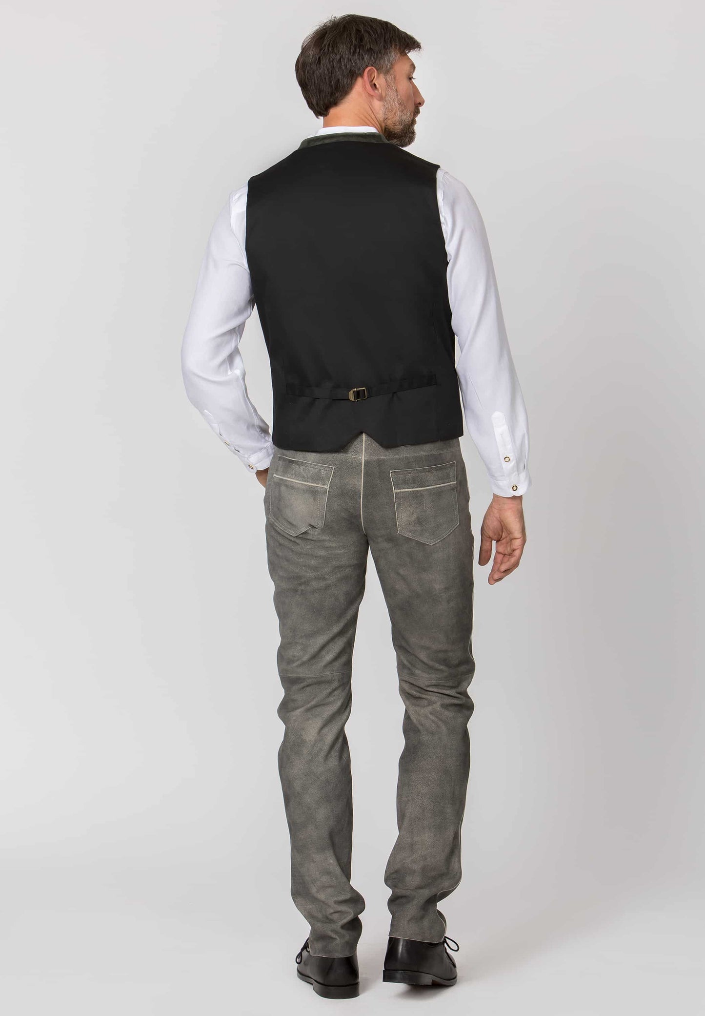 back view Man wearing a green vest over a white shirt with gray leather lederhosen pants on a white background