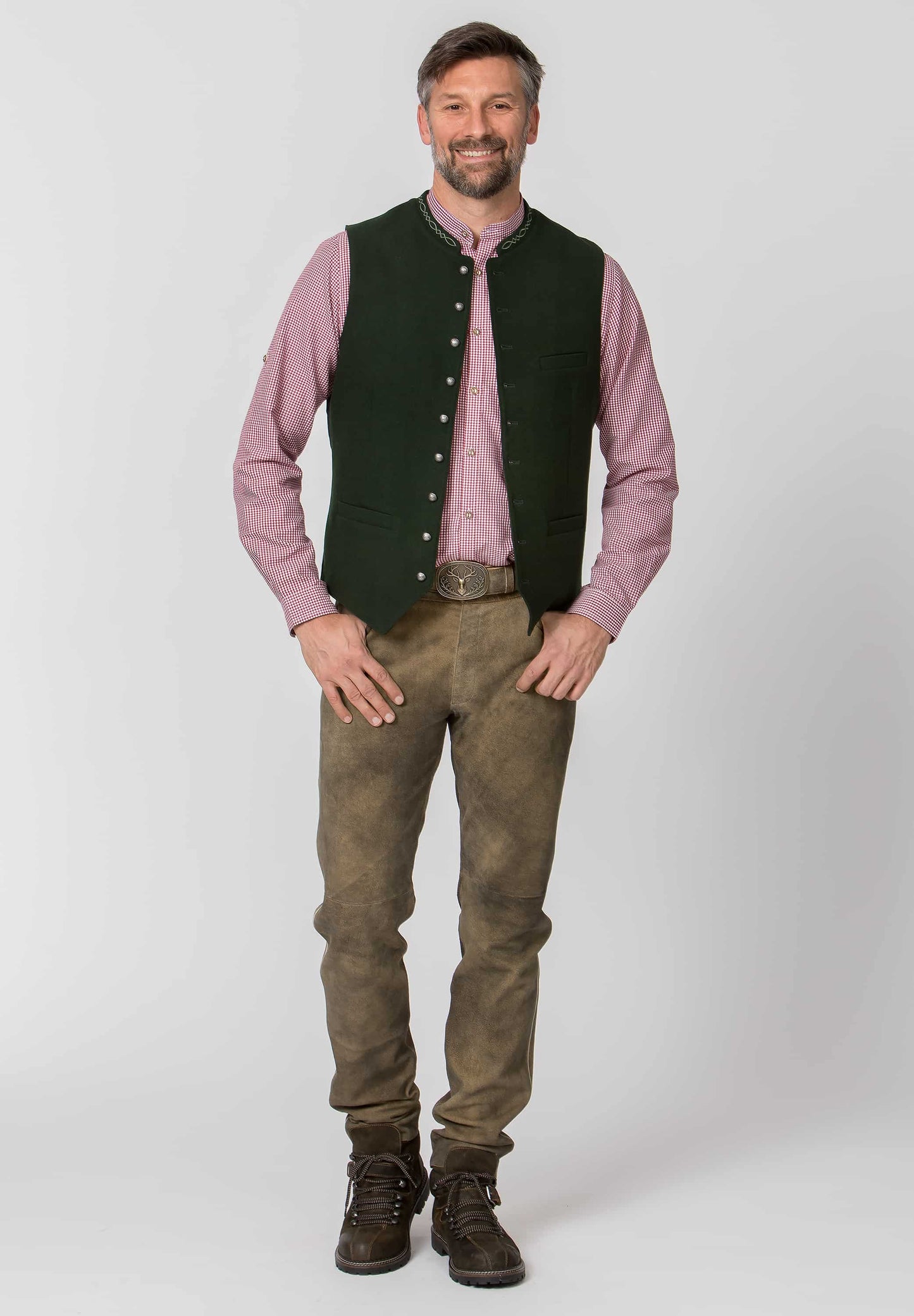 Man wearing a pink shirt, black vest, Long leather brown pants, and boots on a white background