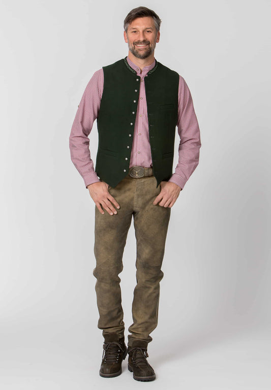 Man wearing a pink shirt, black vest, Long leather brown pants, and boots on a white background