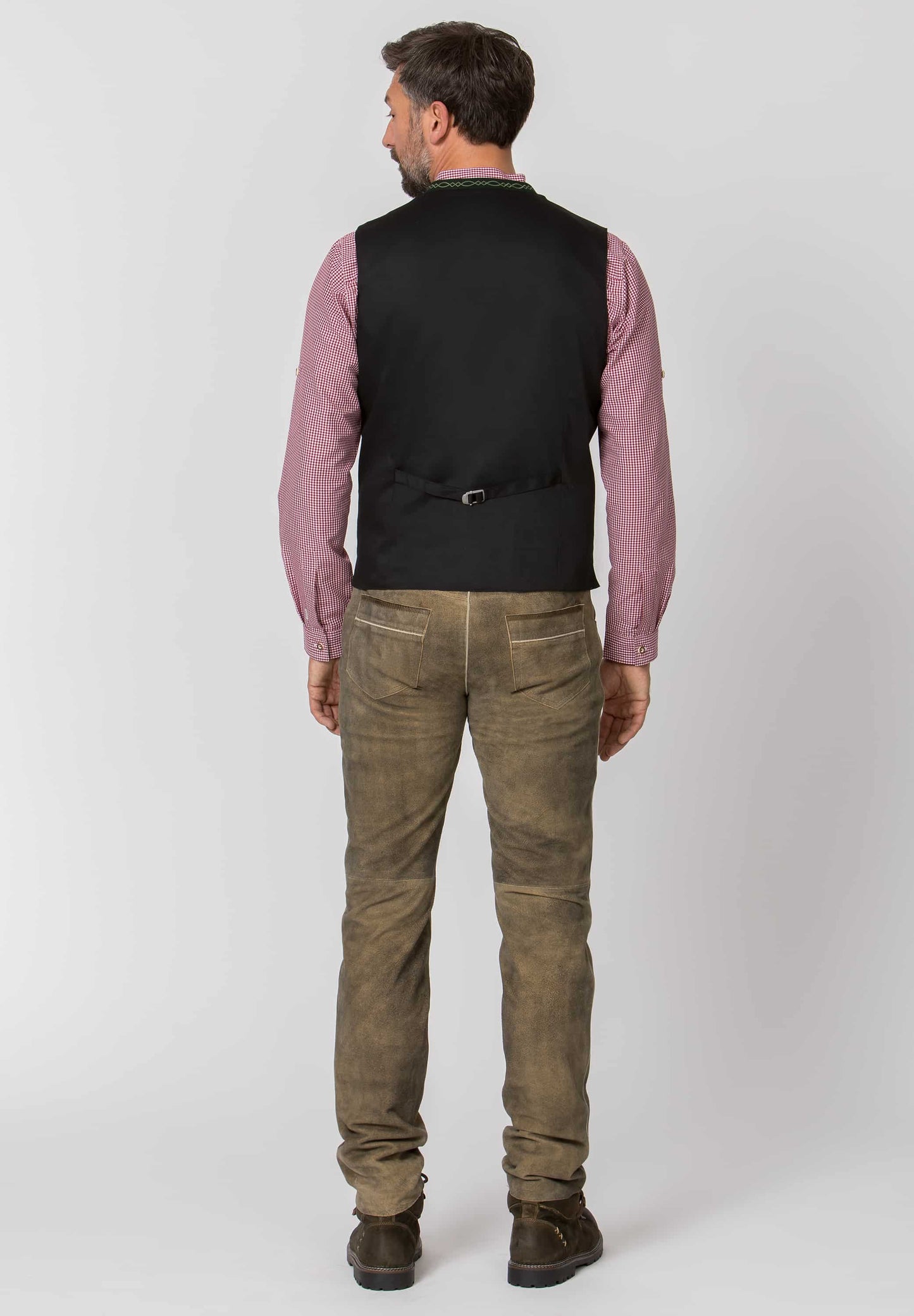 back view of Man wearing a pink shirt, black vest, Long leather brown pants, and boots on a white background