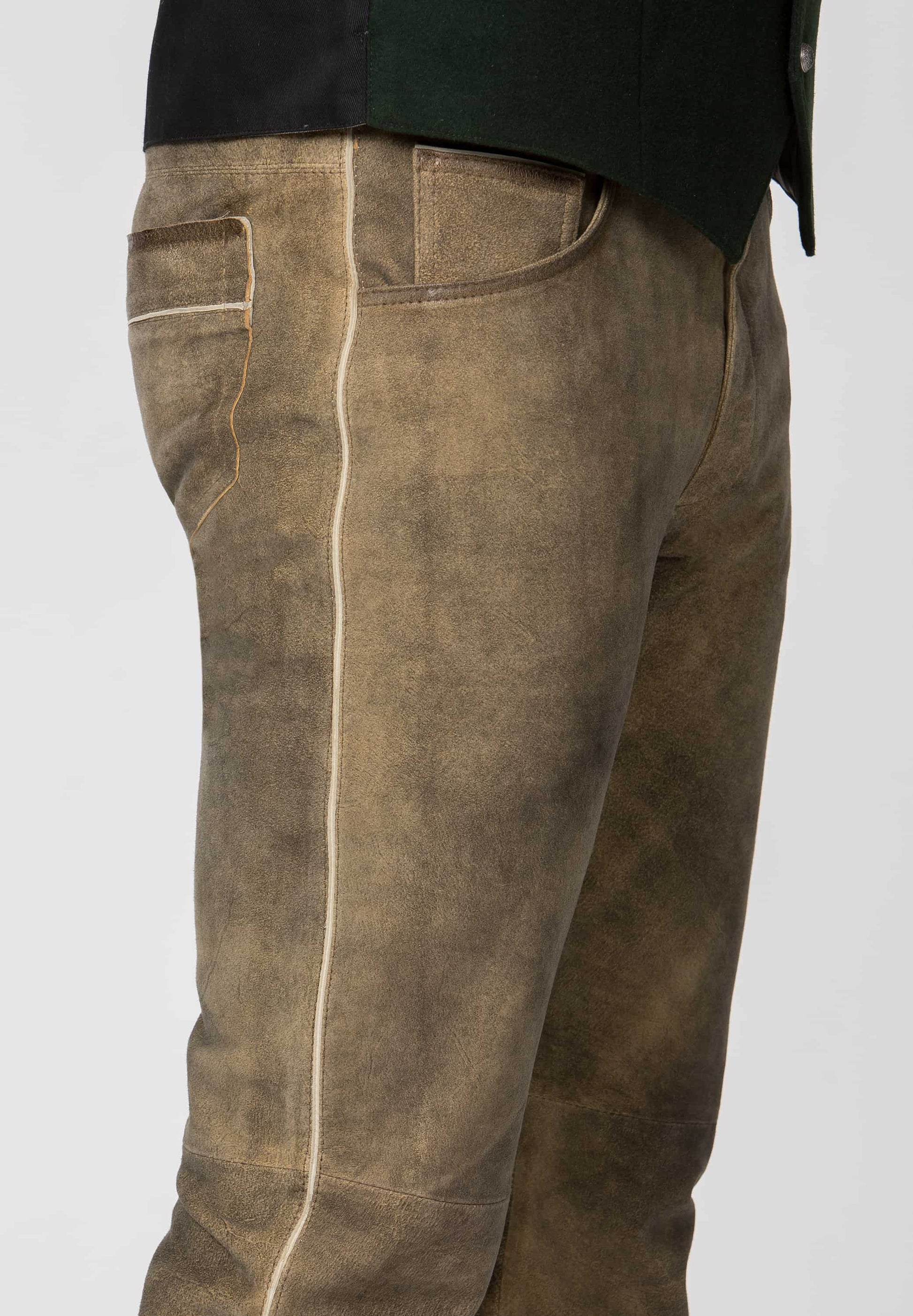 side view of Man wearing a pink shirt, black vest, Long leather brown pants, and boots on a white background