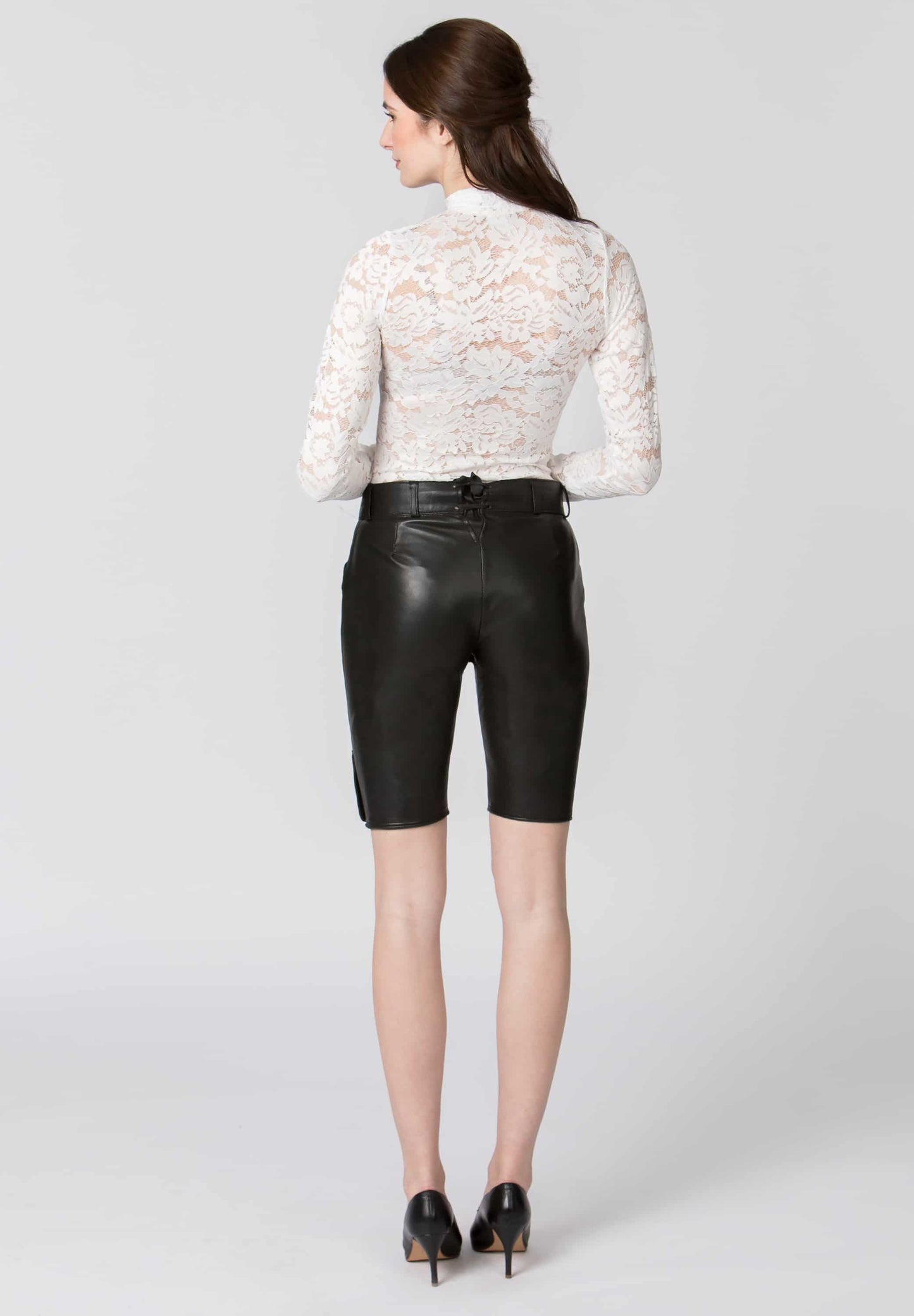 A backview of a woman wearing a white lace top and black leather shorts on a white background