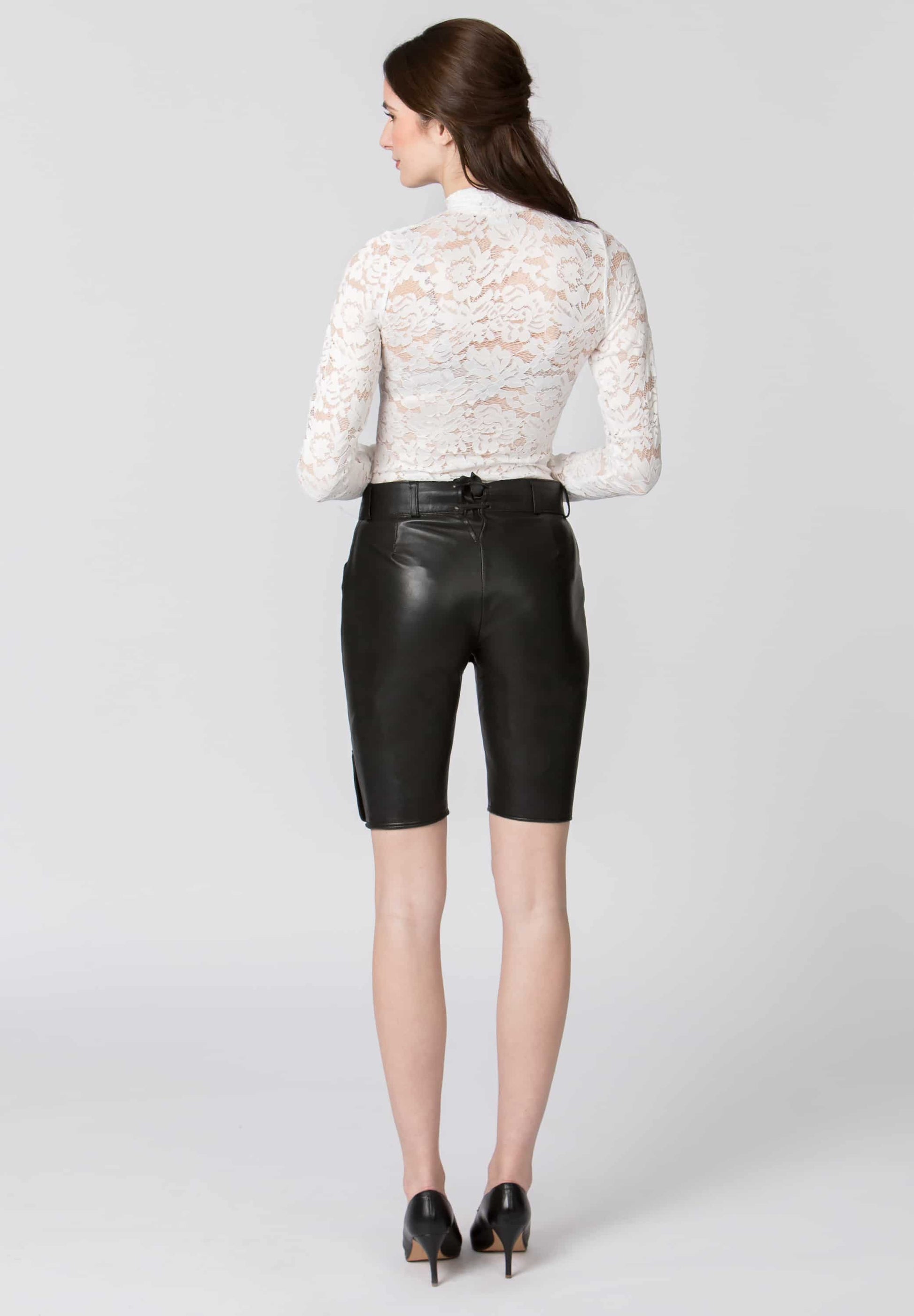 A backview of a woman wearing a white lace top and black leather shorts on a white background