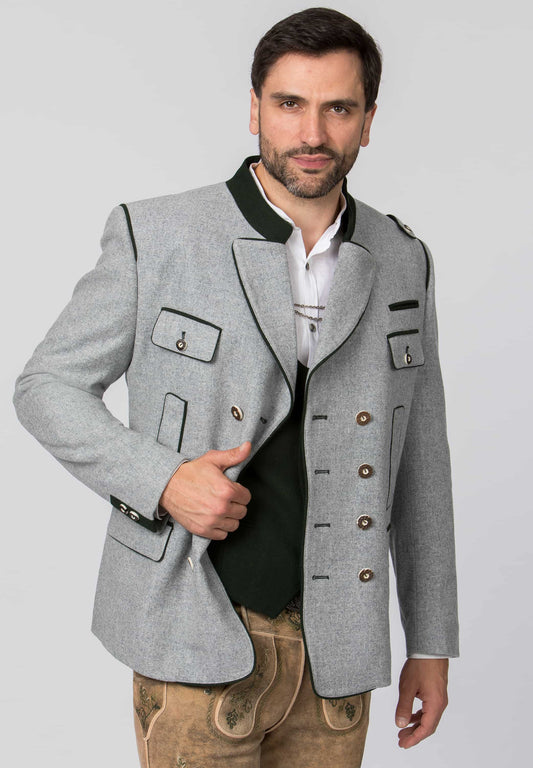 A man modeling a light gray traditional Bavarian-style jacket with black trim, brown buttons, and a white shirt underneath, paired with tan leather pants, against a solid light gray background.