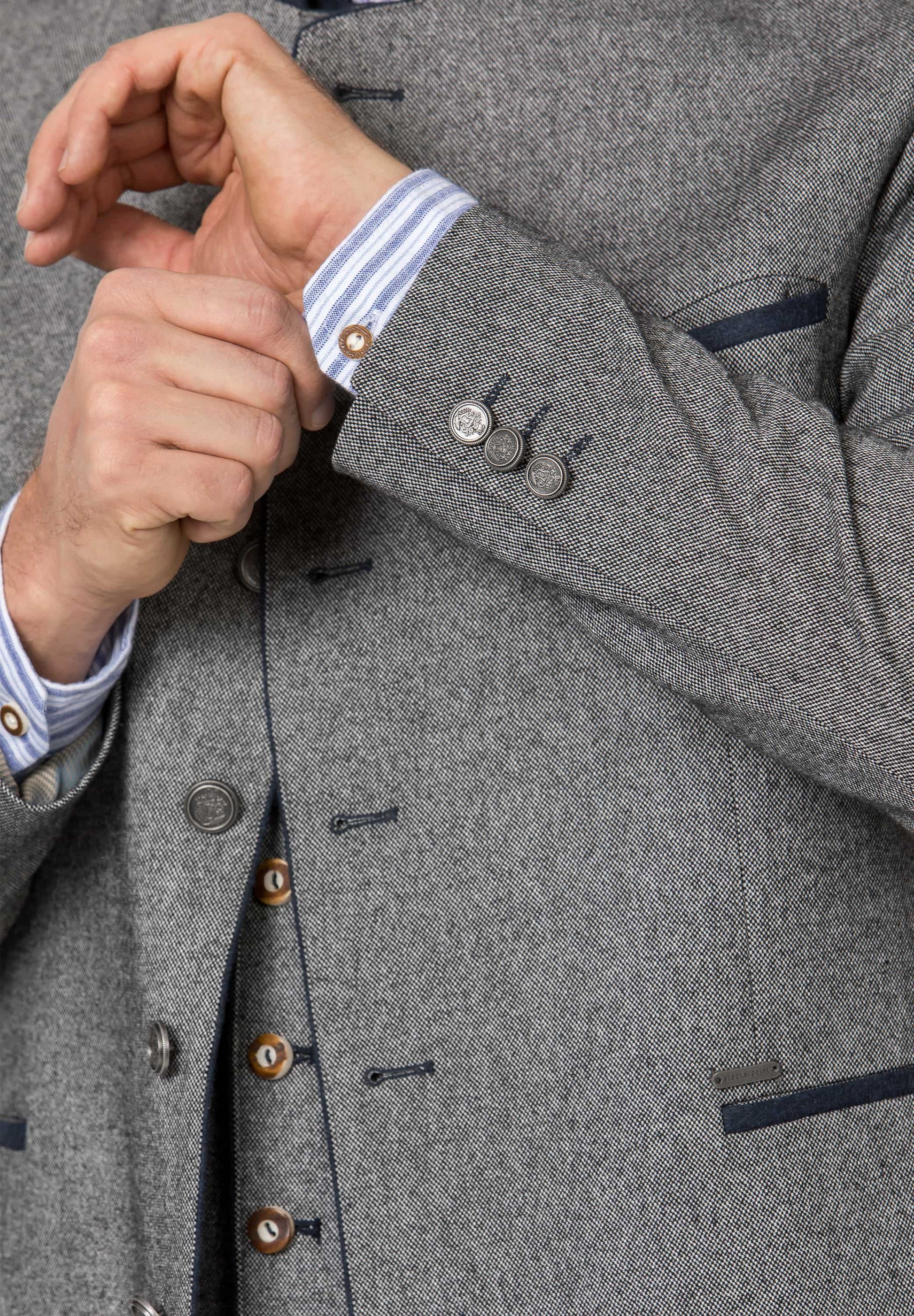 Close-up of a gray coat with button details and a striped shirt cuff.