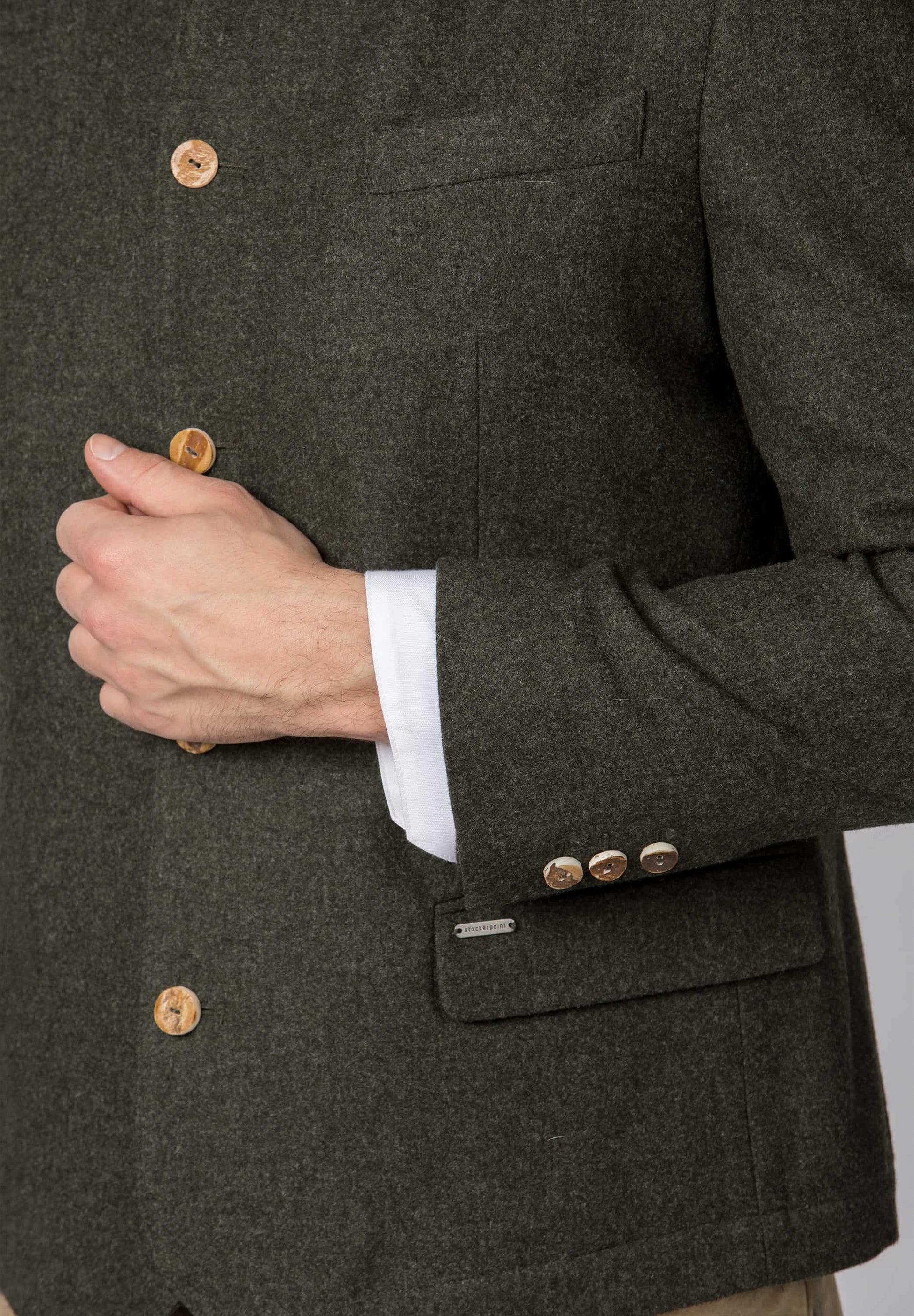 Close-up of a person wearing a dark green textured jacket with buttons and a white shirt cuff.