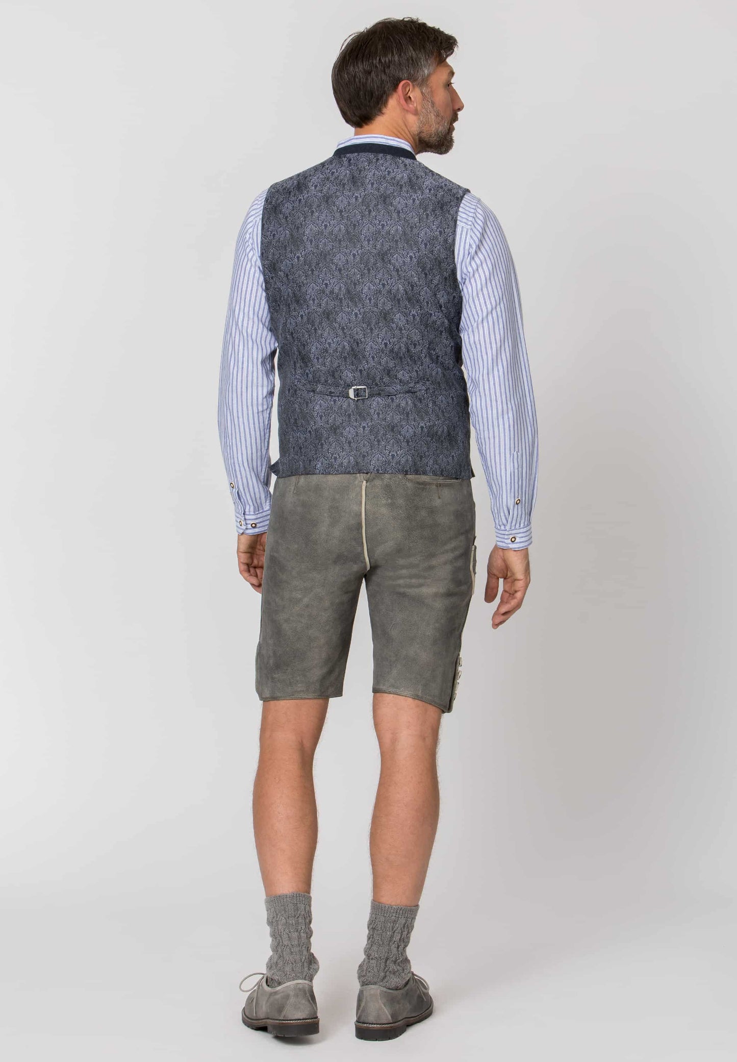 Man wearing a patterned vest, striped shirt, and shorts on a white background