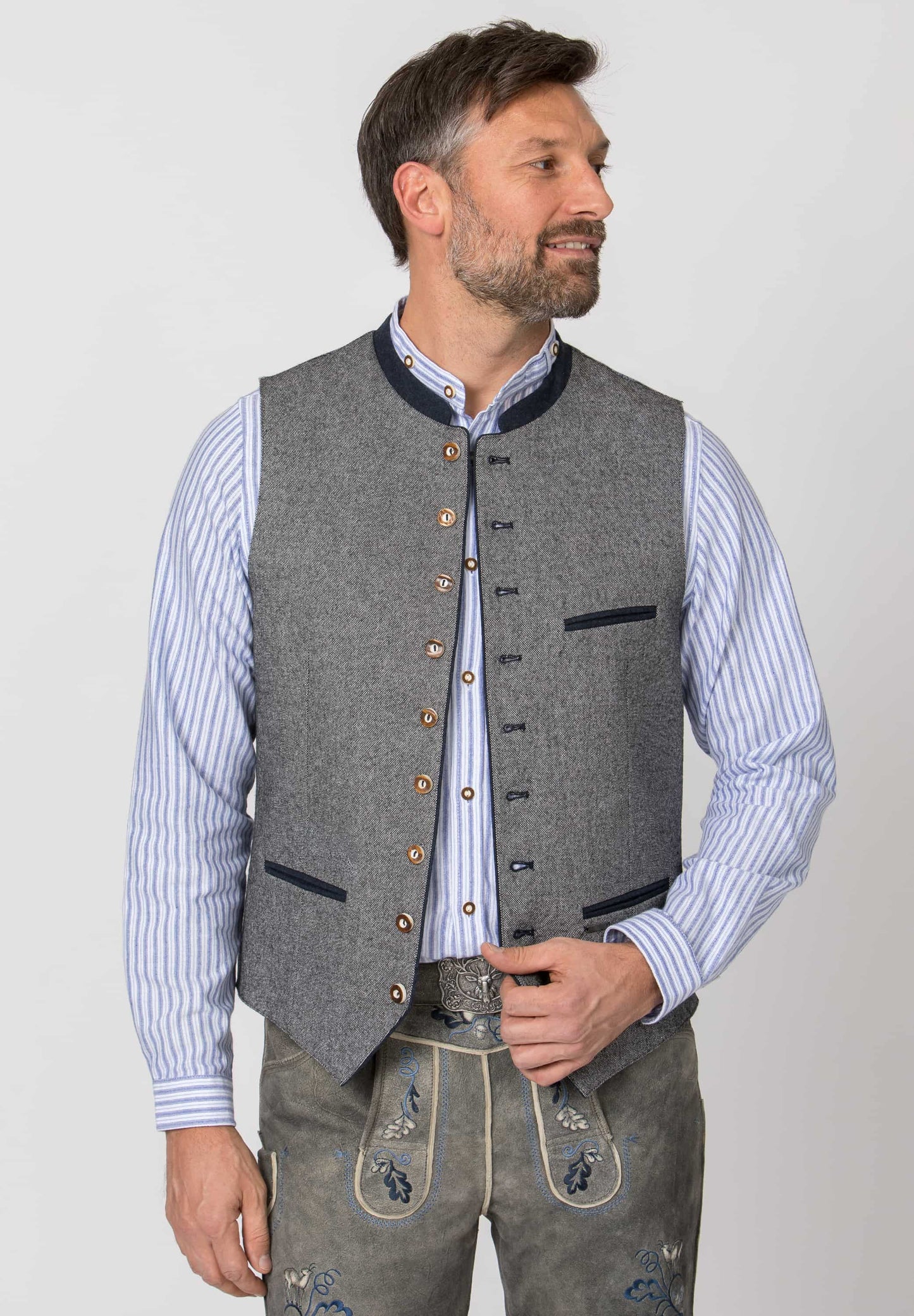 A man wearing a gray wool-like button-front vest over a light blue and white striped shirt, paired with gray embroidered traditional-style trousers, photographed against a light gray studio background.