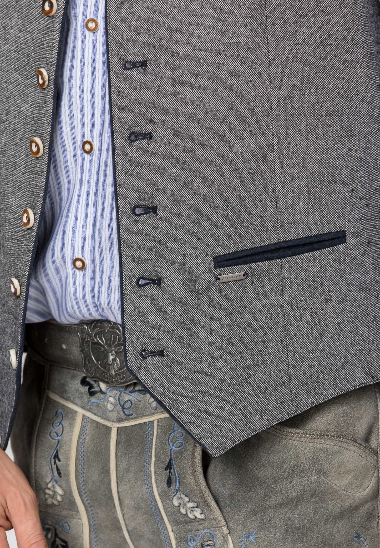 Close-up of a gray wool-like vest or jacket worn over a blue-and-white striped shirt, with embroidered gray pants and a silver belt visible below.