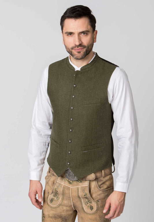 Man wearing a green vest over a white shirt with brown pants on a light gray background