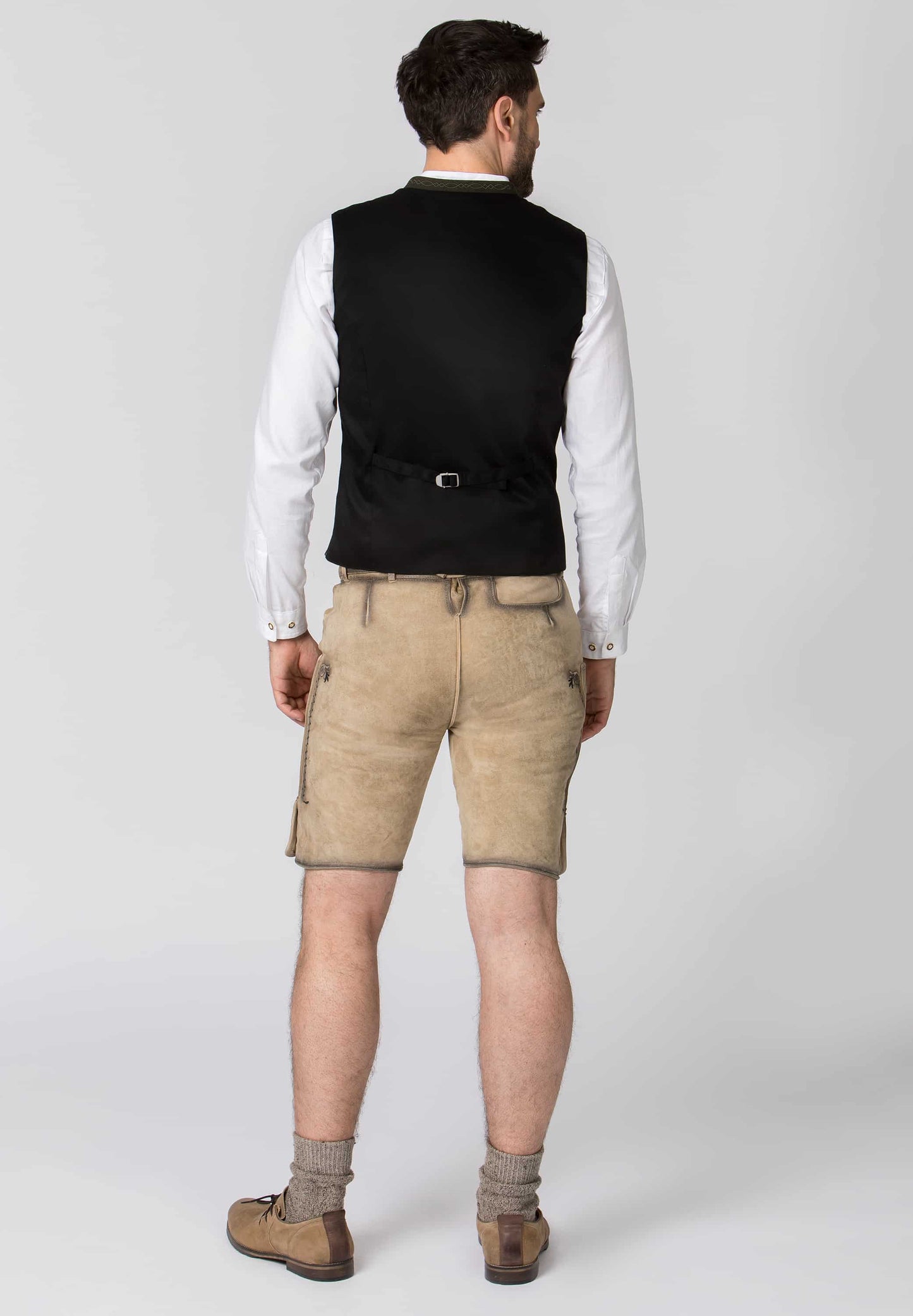 Man wearing a black vest, white shirt, beige shorts, and brown shoes on a white background