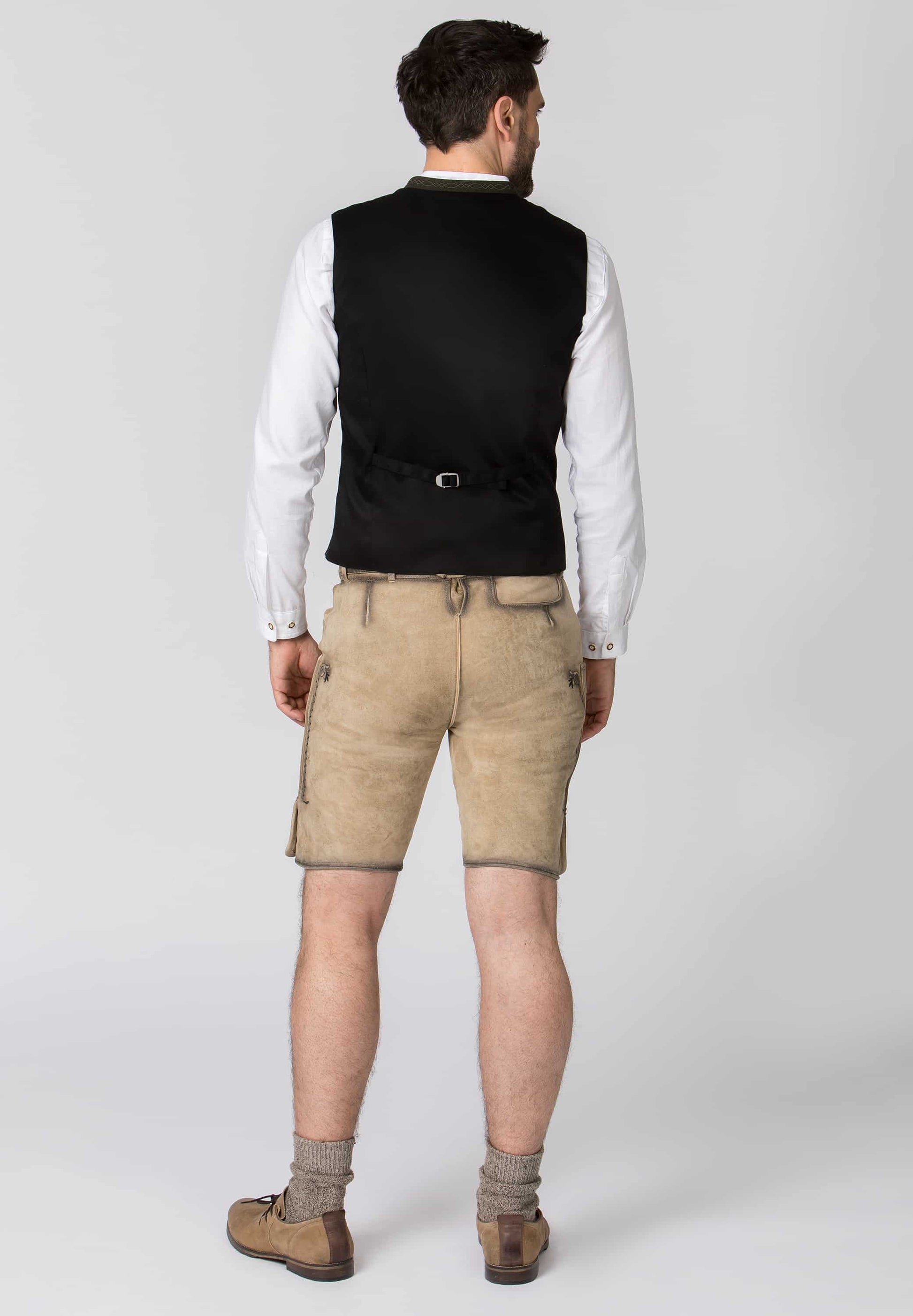 Man wearing a black vest, white shirt, beige shorts, and brown shoes on a white background