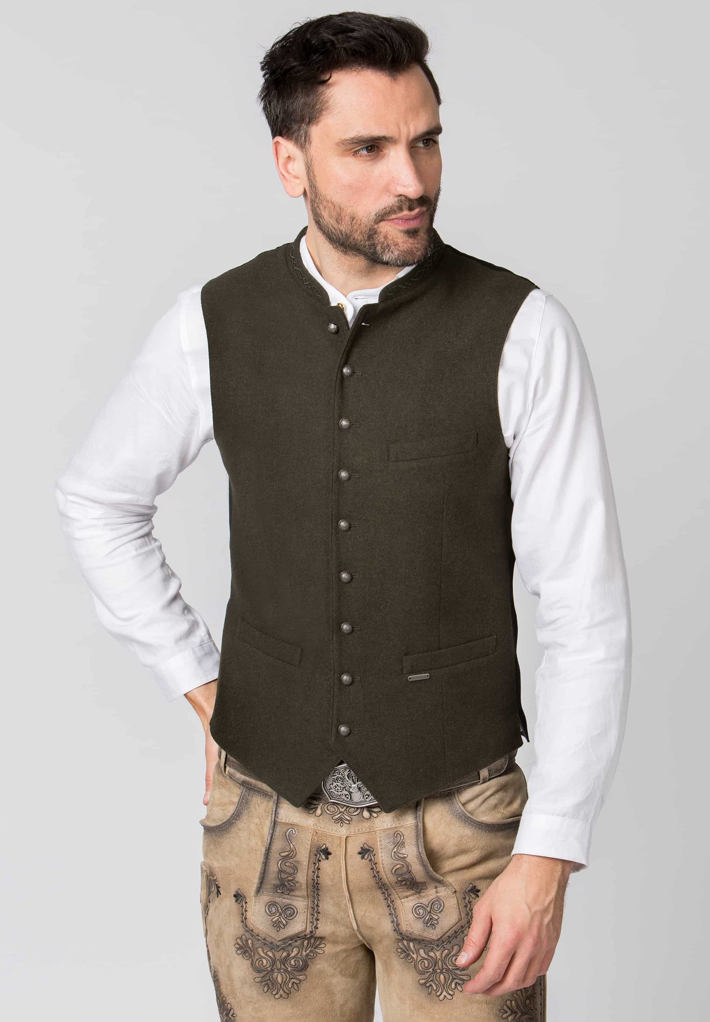 Man wearing a brown vest over a white shirt with beige pants on a gray background