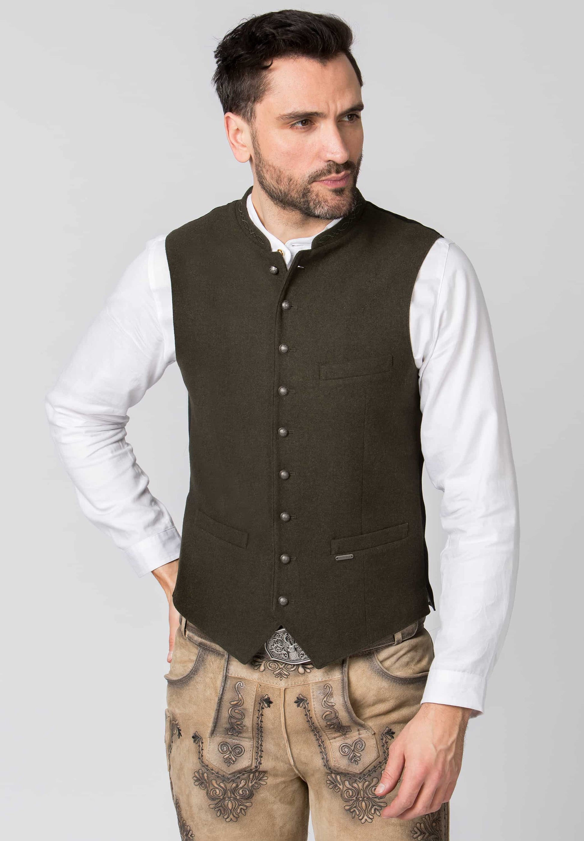 Man wearing a brown vest over a white shirt with beige pants on a gray background