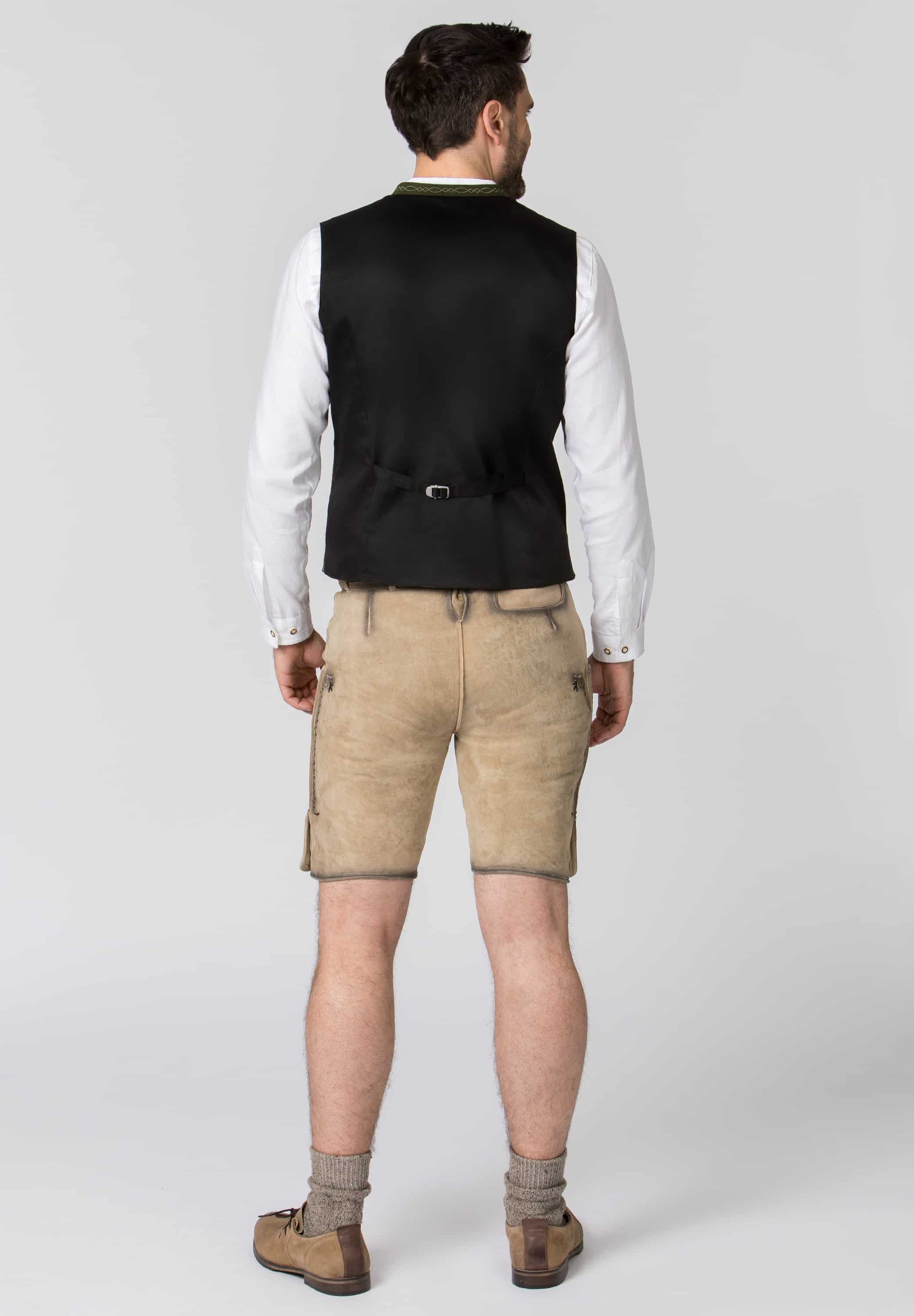 Man wearing a black vest, white shirt, beige pants, and brown shoes on a white background