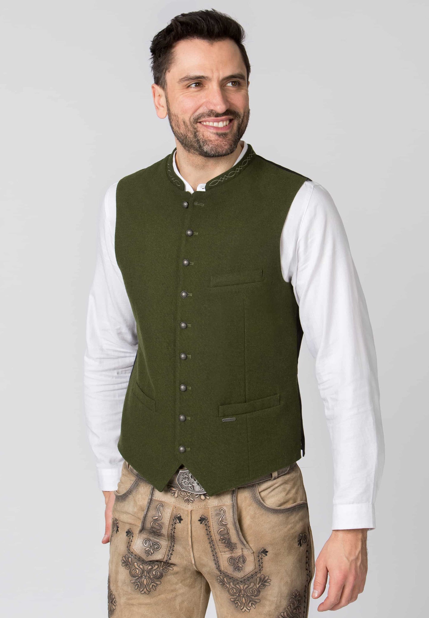 Man wearing a green vest over a white shirt with a plain background