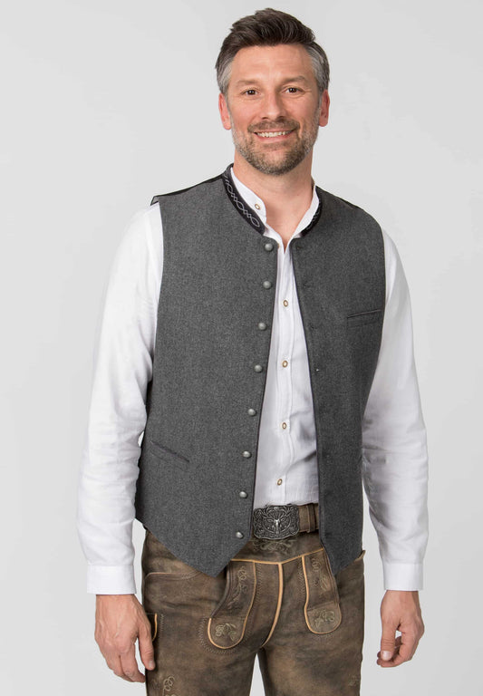 Man wearing a gray vest over a white shirt with brown pants on a light gray background