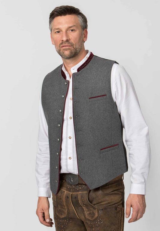 Man wearing a gray vest over a white shirt with brown pants on a light gray background