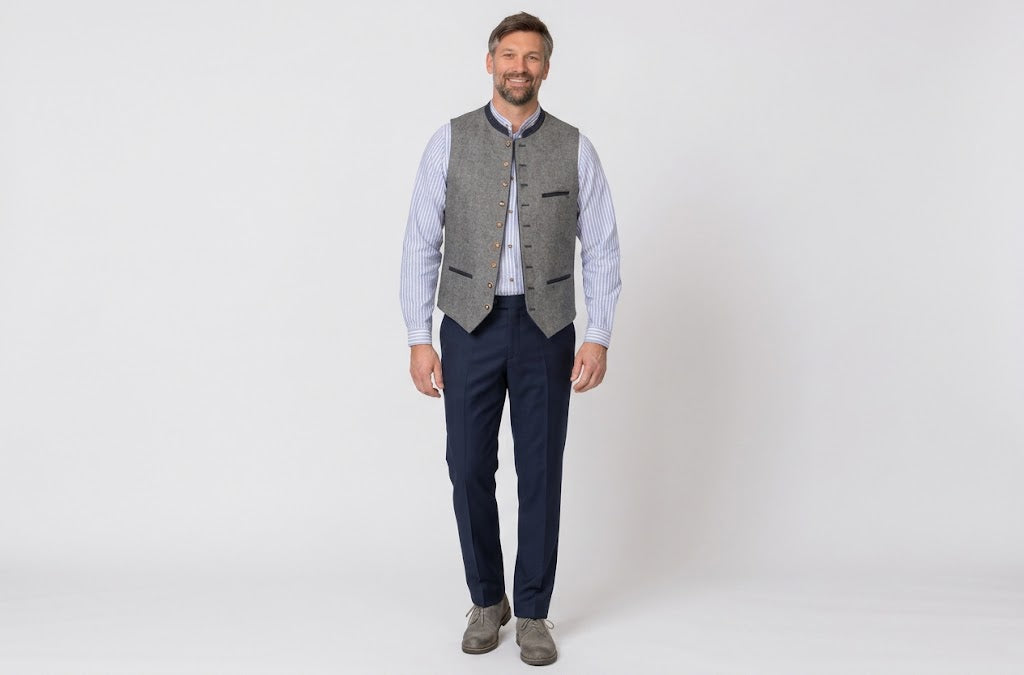 A man modeling a grey textured waistcoat vest over a light blue dress shirt, paired with navy trousers and grey suede shoes, standing against a plain white studio background.
